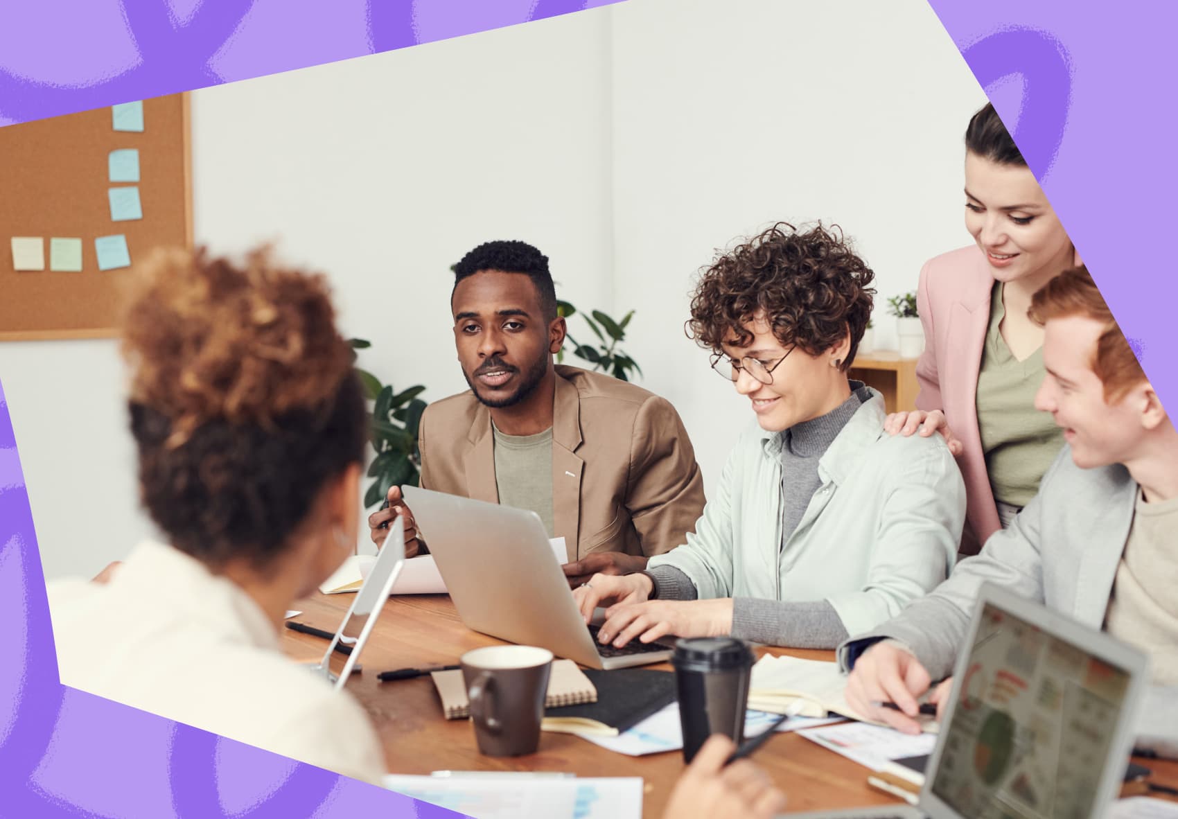 Colleagues sitting at a table in a meeting. One woman is on her laptop