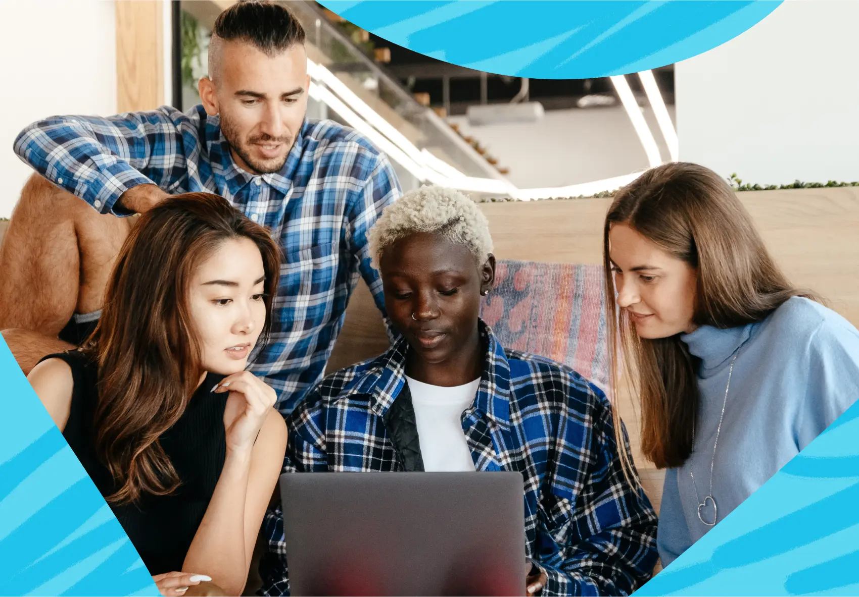 A woman sitting in front of a laptop at work with three co-workers sitting next to her looking over her shoulder